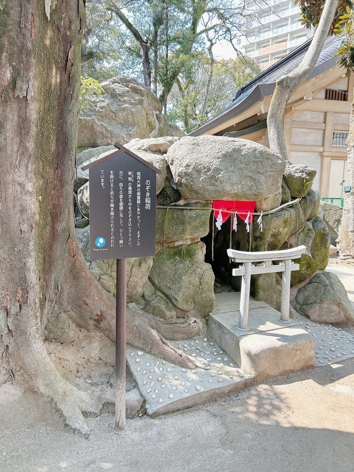 A small Inari shrine tucked beneath mossy rocks, with a stone torii